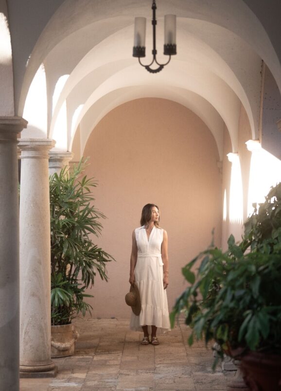 Woman in courtyard with arched architecture.